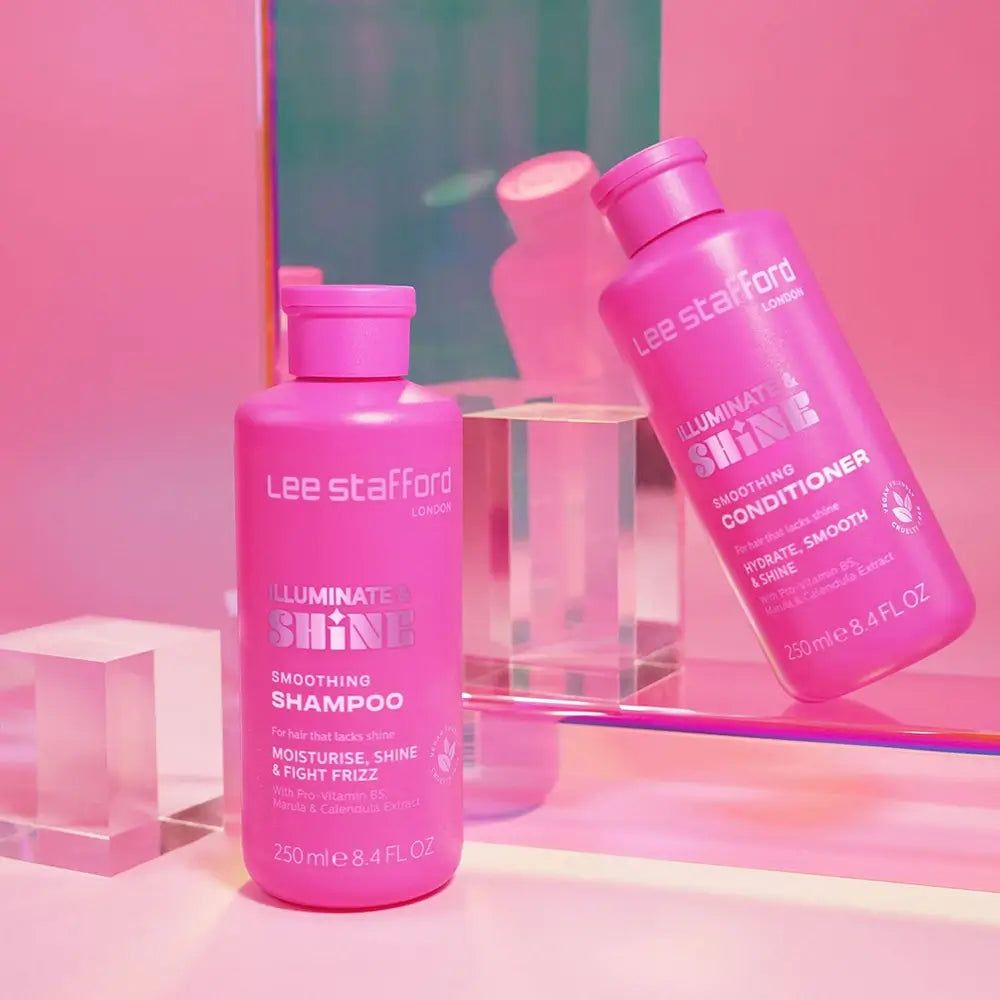 Twee roze flessen Lee Stafford producten, een conditioner en een shampoo, op een glazen oppervlak.