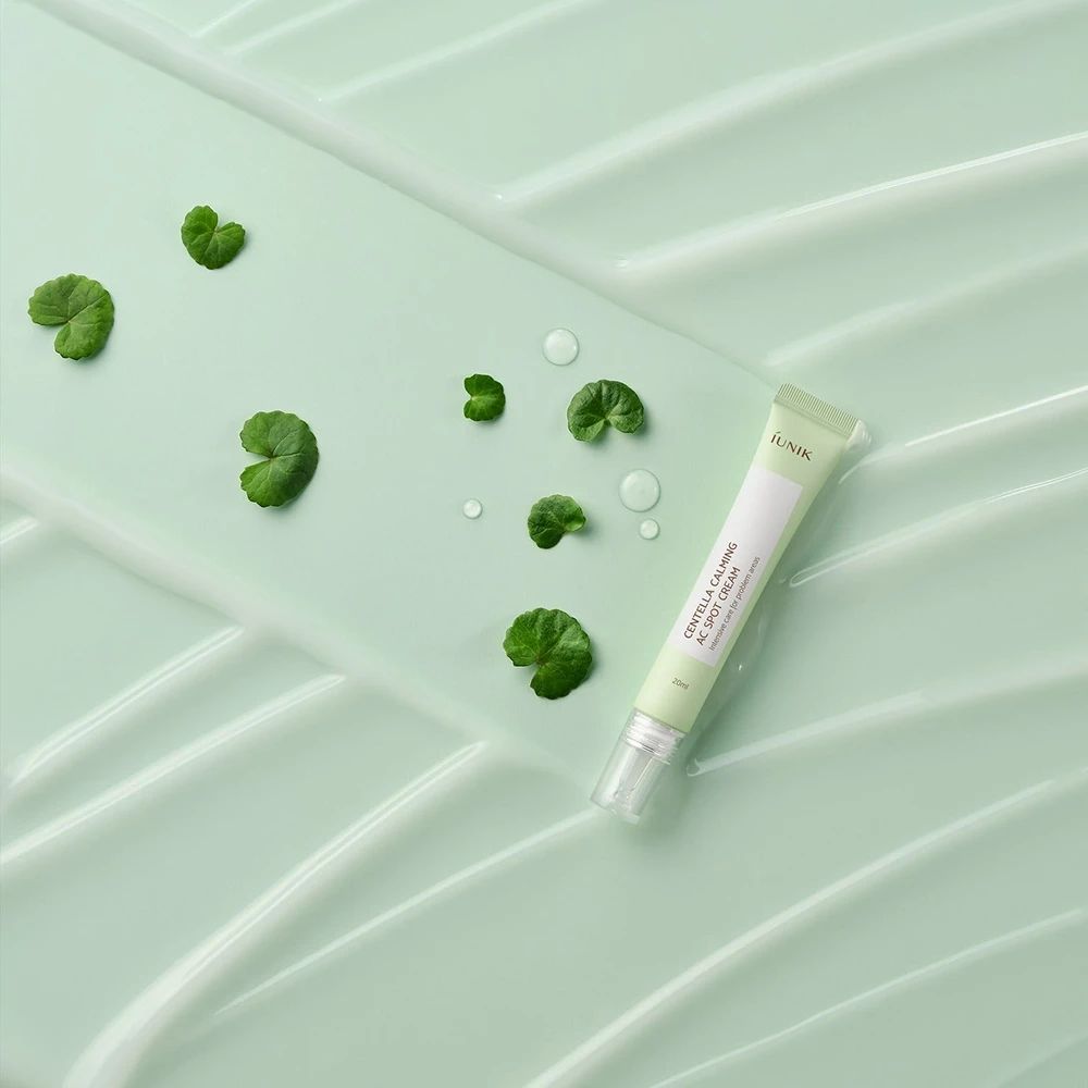 Tube verte sur fond vert avec feuilles et gouttes d'eau. Inscription : iUNIK, Centella Calming AC Spot Cream.