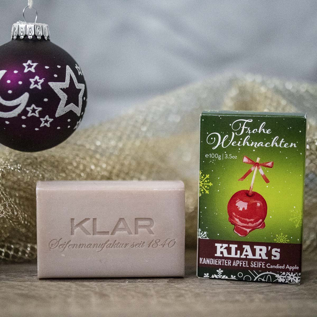 Zeepblok met opschrift "KLAR" en verpakking met appelmotief. Kerstdecoratie op de achtergrond.
