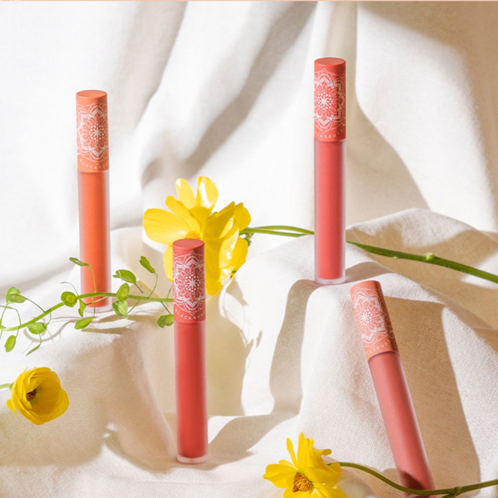 Vier lipsticks met bloemmotieven op de dop, op wit doek, met gele bloemen.