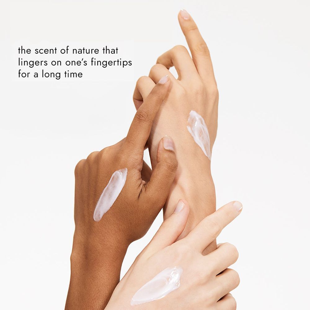 Mains avec crème. Appliquée sur deux mains. Texte: Le parfum de la nature qui s'attarde longtemps sur les doigts.
