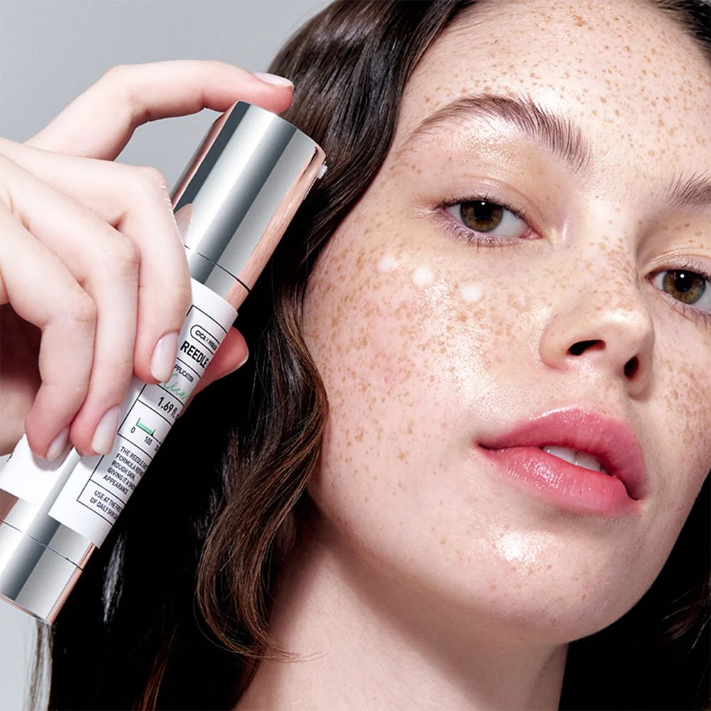 Une femme tient une ampoule VT Cosmetics Reedle Shot devant son visage avec l'essence appliquée.