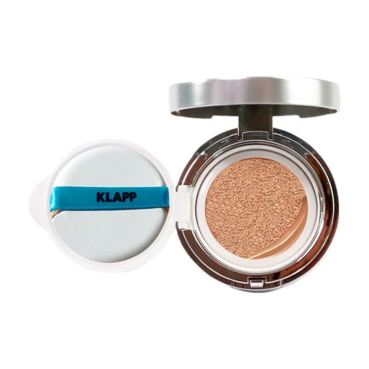 Klapp Hyaluronic Cushion. Ronde, open doos met spons en getint product. Zilverkleurig deksel, witte spons met blauwe band.