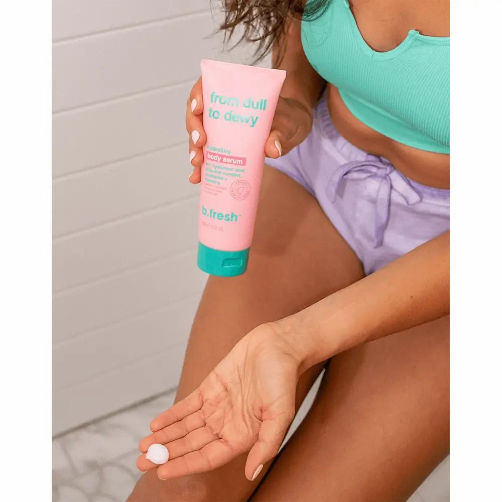 Personne tenant un tube rose avec bouchon turquoise. Inscription : From Dull To Dewy. Produit appliqué sur la main.