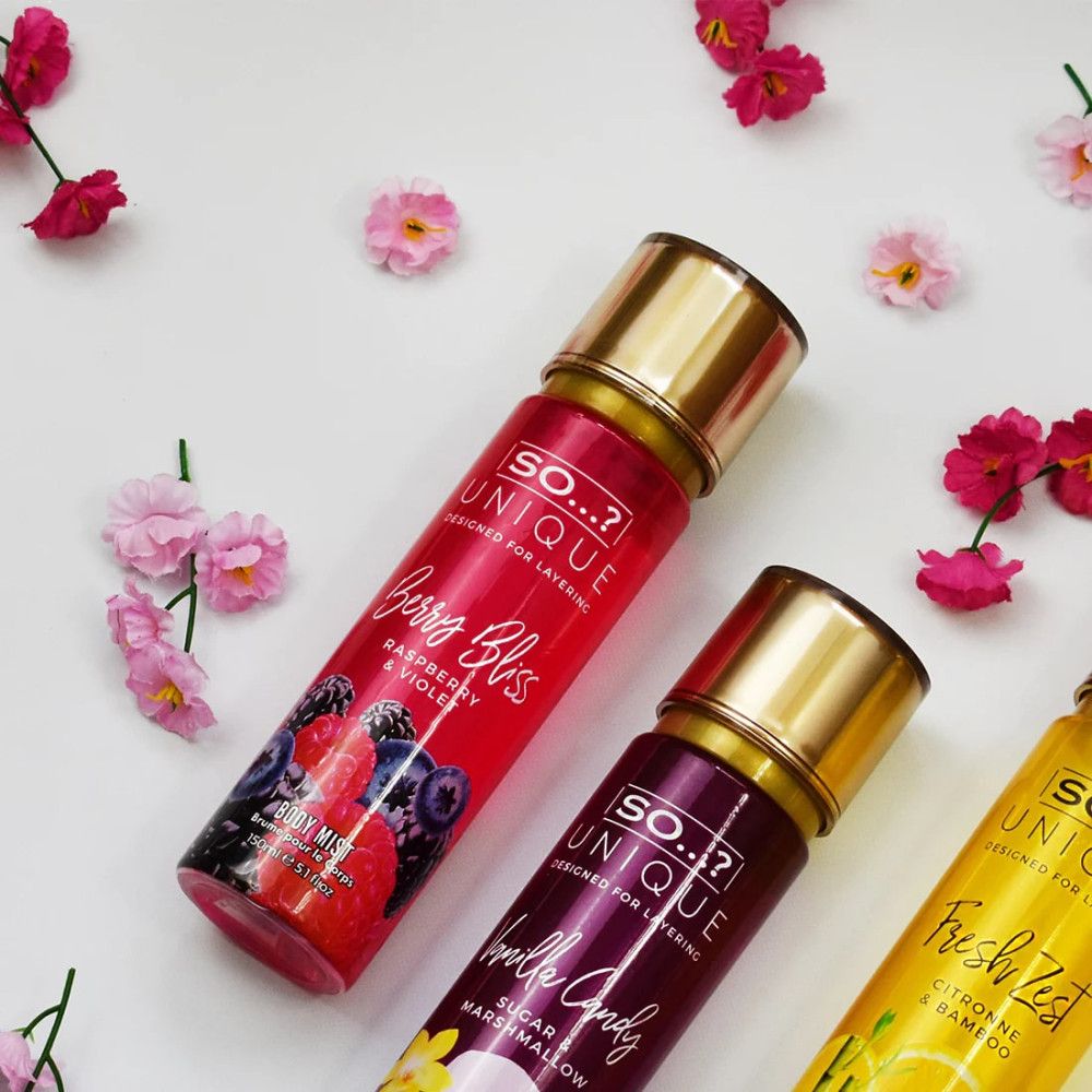 Drie body mist flessen met gouden doppen. Opschrift: So Unique. Producten: Berry Bliss, Vanilla Candy, Fresh Zest. Omringd door bloemen.
