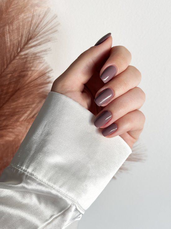 Main avec ongles vernis N8 Tinted Taupe. Chemise blanche. Fond: décoration marron.