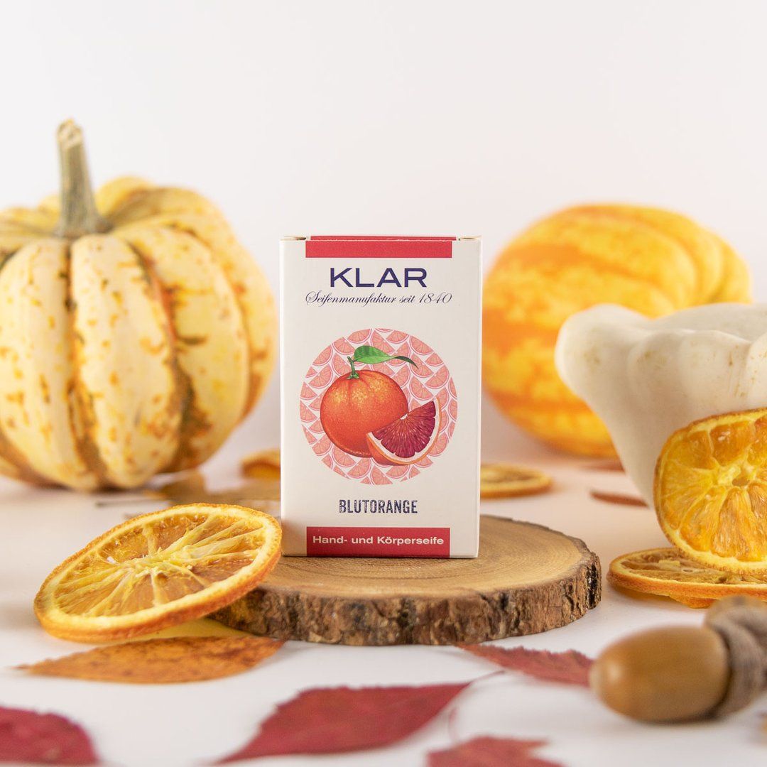 Verpakking op houten schijf. Bloedsinaasappel illustratie. Tekst: KLAR, Blutorange, hand- en lichaamszeep. Decoratie: pompoenen, bladeren, sinaasappelschijfjes.