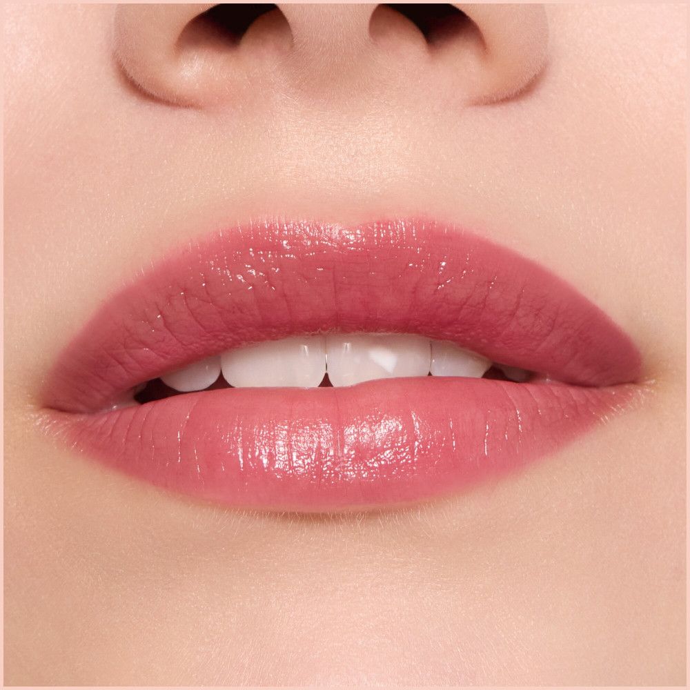 Gros plan sur des lèvres avec du baume à lèvres. Lèvres teintées de rose, brillantes. Dents visibles.