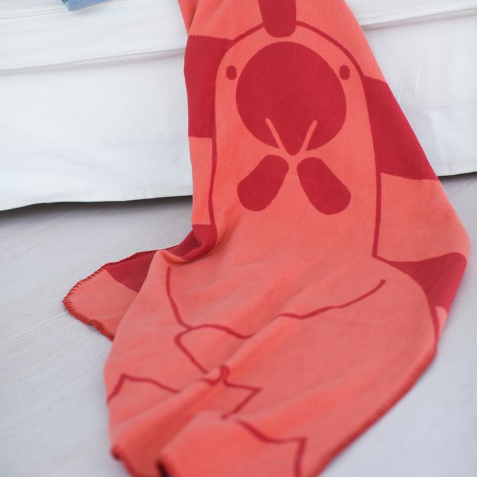 Rode deken met kippenontwerp. Getoond op wit bed. Detail van de stof.