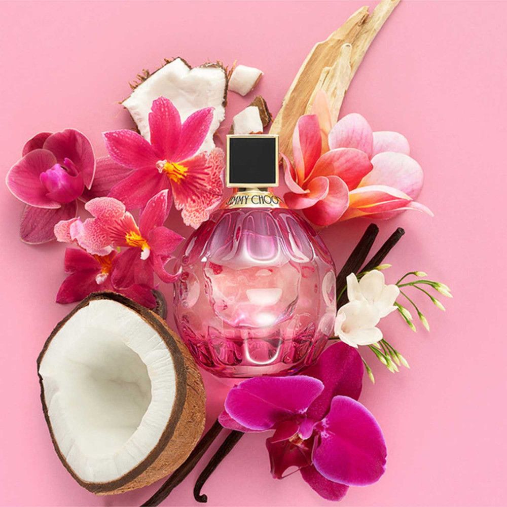 Roze Jimmy Choo Rose Passion fles, omringd door bloemen, kokosnoot en vanillestokjes. Ronde, roze fles met zwarte dop.