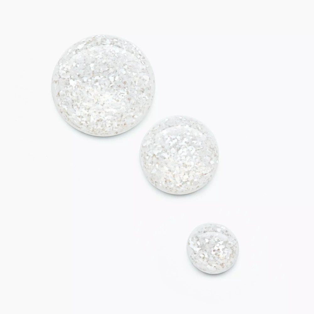 Trois objets ronds et scintillants. Fond blanc. Particules scintillantes de différentes tailles.