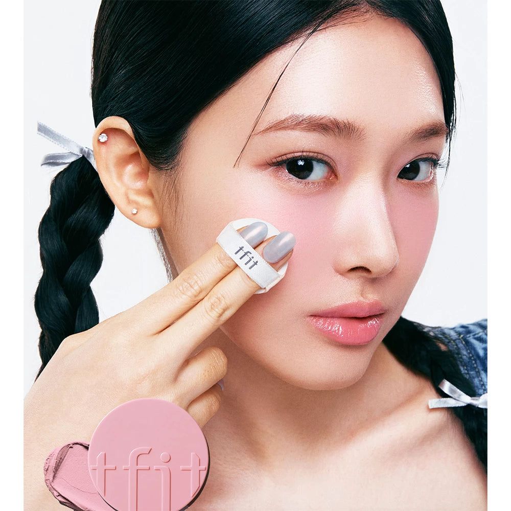 Person appliquant le blush TFIT Fluffy Velvet Cushion avec une houppette. Fard à joues rose visible sur la joue. Nom du produit sur l'applicateur.