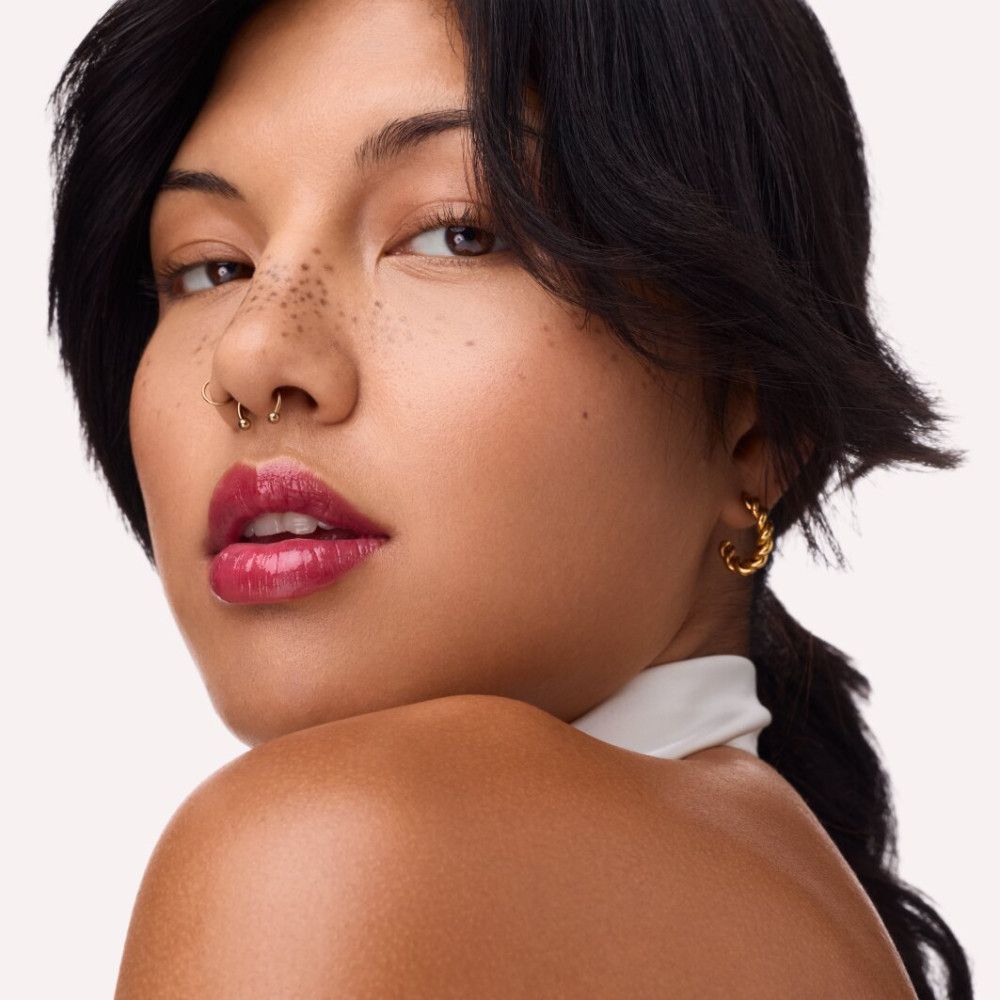 Portret van een vrouw met rode lipgloss. Zichtbare lippen, neuspiercing, oorbellen.