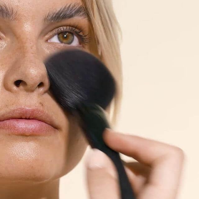 Personne appliquant de la poudre sur le visage avec un pinceau. Gros plan. Fond clair.
