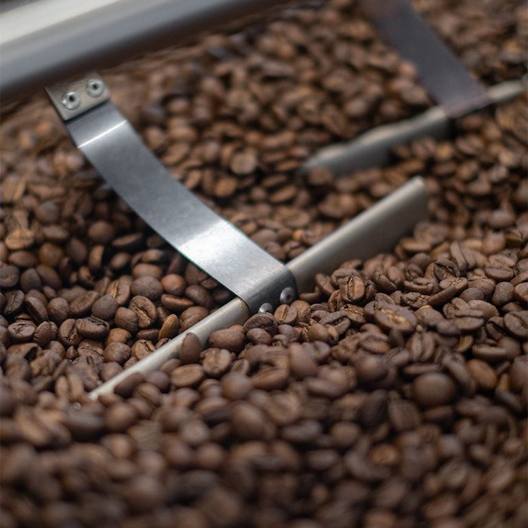 Koffiebonen in een brander. Metalen armen bewegen door de bonen. Close-up.