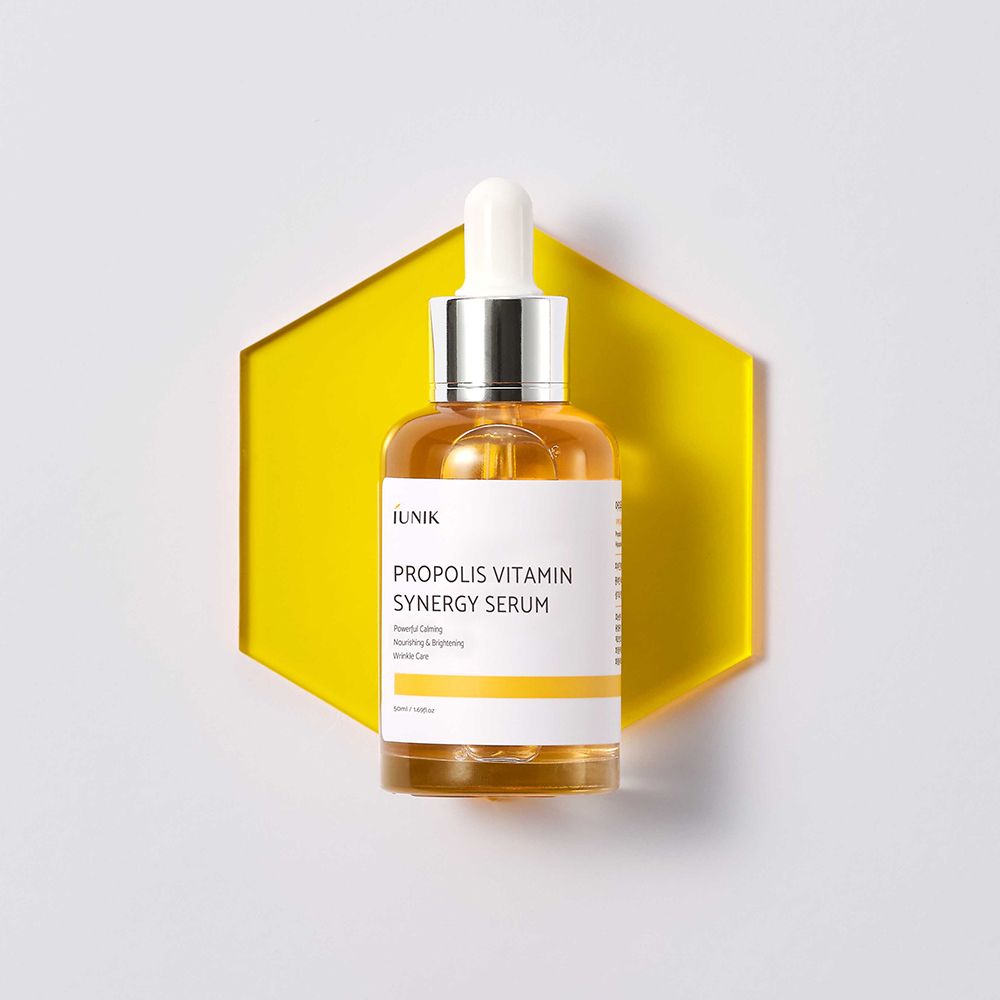 Serumfles met pipet op gele zeshoekige achtergrond. Opschrift: iUNIK Propolis Vitamin Synergy Serum.