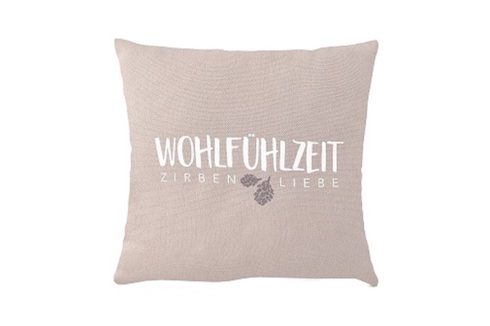 Coussin beige avec impression. Texte: WOHLFÜHLZEIT ZIRBEN LIEBE. Illustration d'une pomme de pin. Forme carrée.