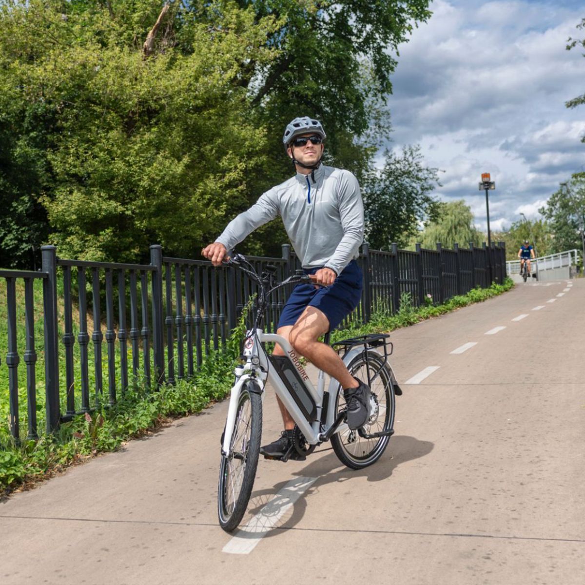 Vélo électrique blanc sur piste cyclable. Cycliste avec casque. Logo JOBOBIKE non visible.