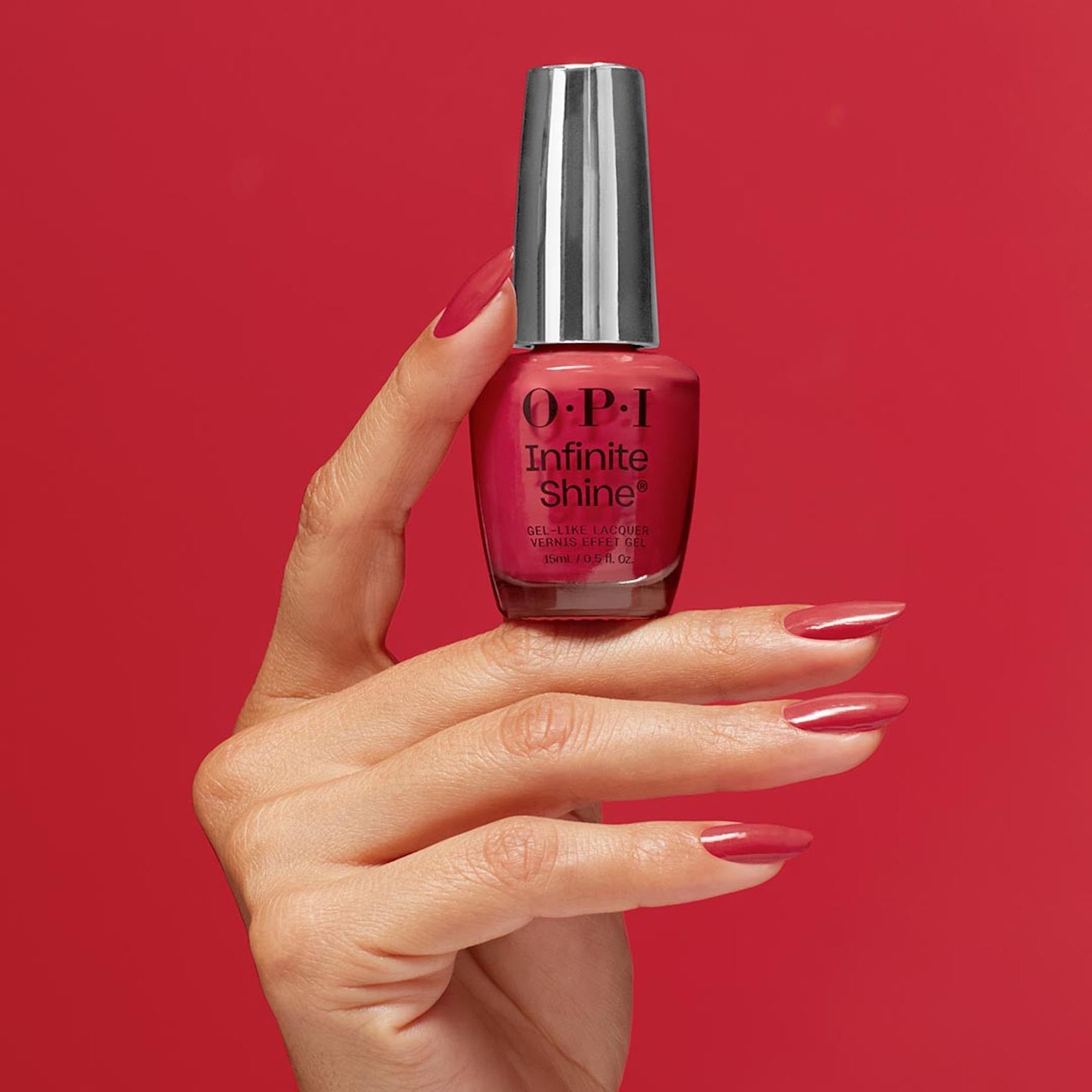 Hand houdt een rode OPI Infinite Shine nagellakfles vast met bijpassende nagels.