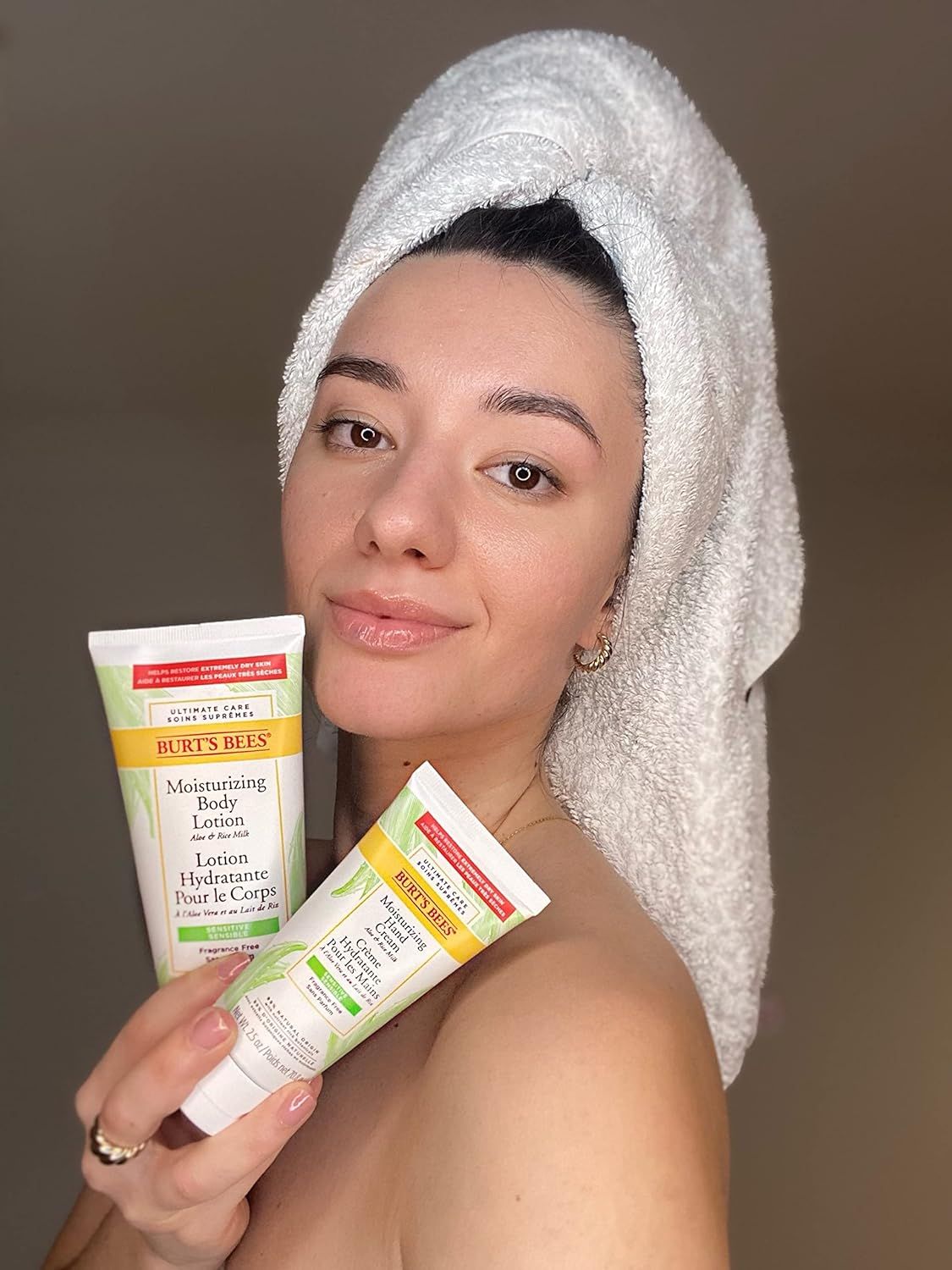 Femme tenant deux tubes de lotion. L'un porte la mention "Burt's Bees". L'autre "Moisturizing Body Lotion".