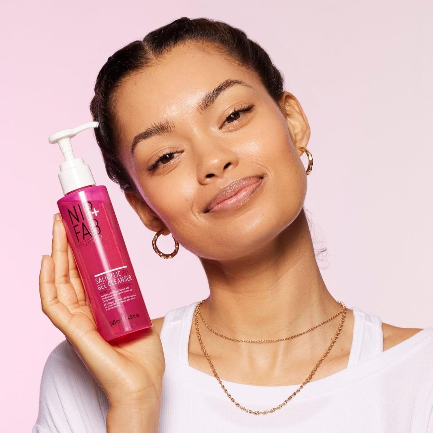Femme tenant un flacon rose. Le flacon porte la marque NIP+FAB et Salicylic Fix Gel Cleanser.