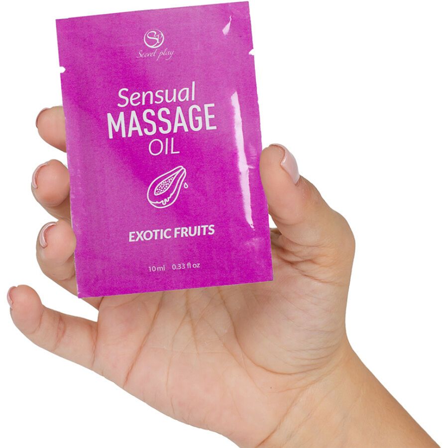 Main tenant un sachet d'huile de massage. Inscription: "Sensual Massage Oil", "Exotic Fruits", logo. Contenu: 10 ml.