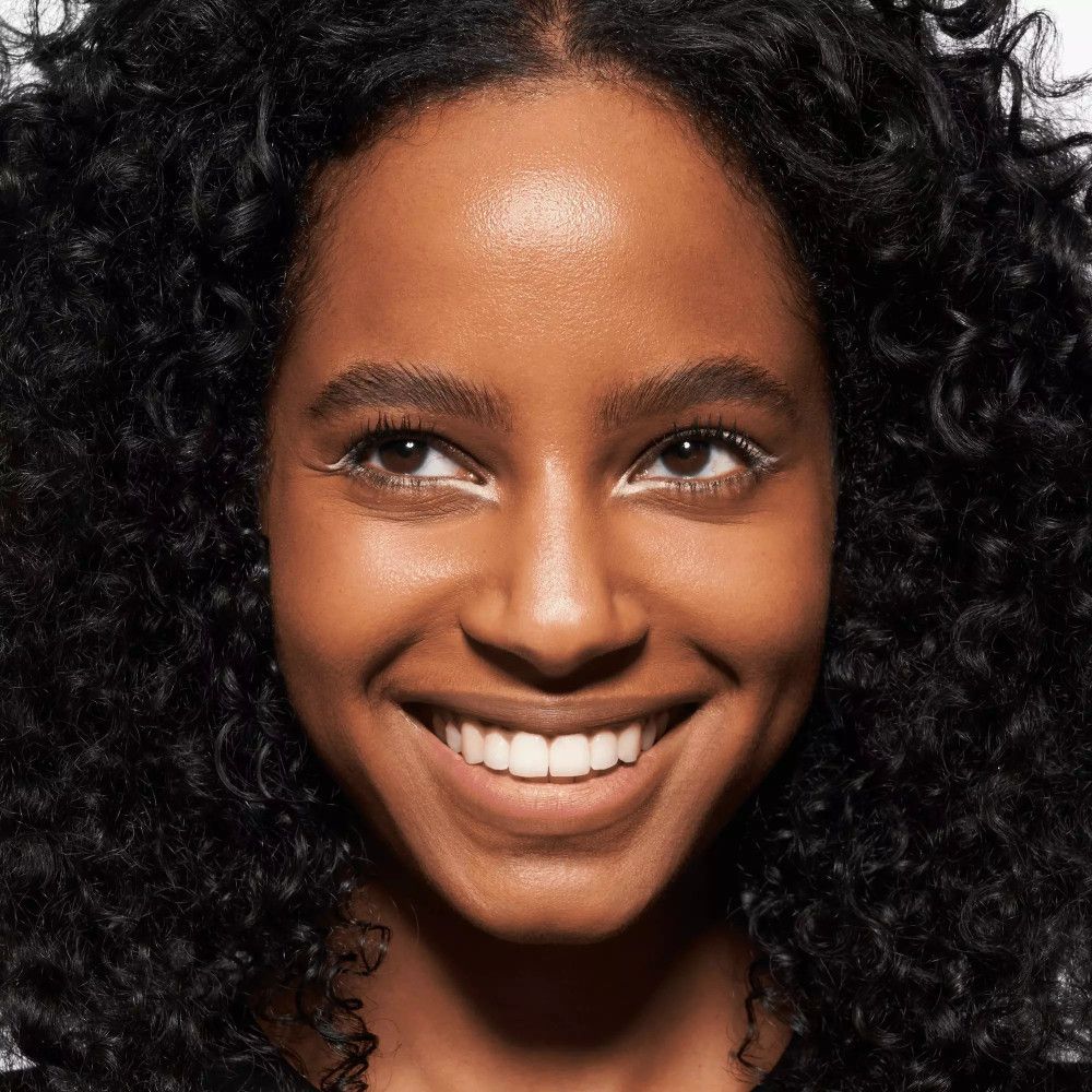 Femme aux cheveux bouclés avec crayon khôl blanc sur la paupière inférieure.