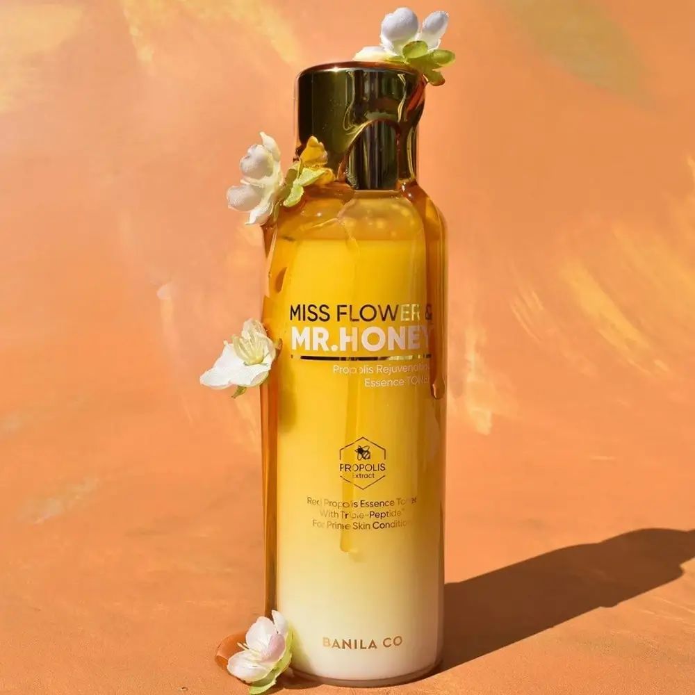 Geel transparante fles met gouden dop. Opschrift: Miss Flower & Mr. Honey, Propolis Rejuvenating Essence Toner. Versierd met bloemen.