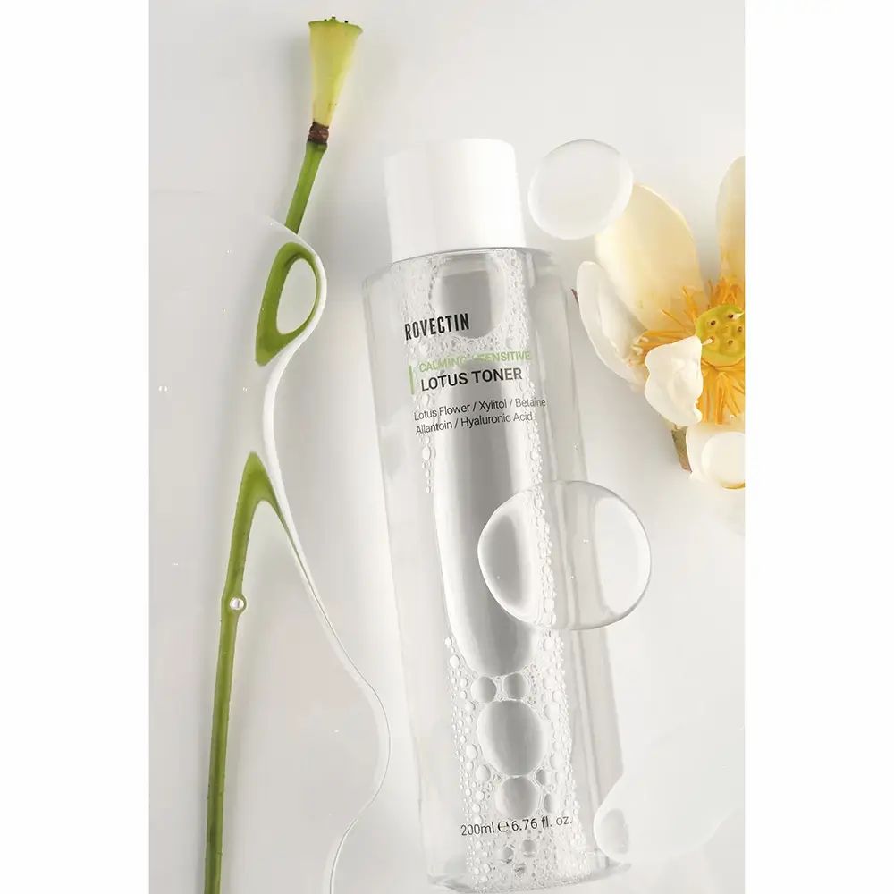 Transparante fles met witte dop. Opschrift: ROVECTIN Calming Lotus Toner. Naast de fles: lotusbloem, steel en waterdruppels.