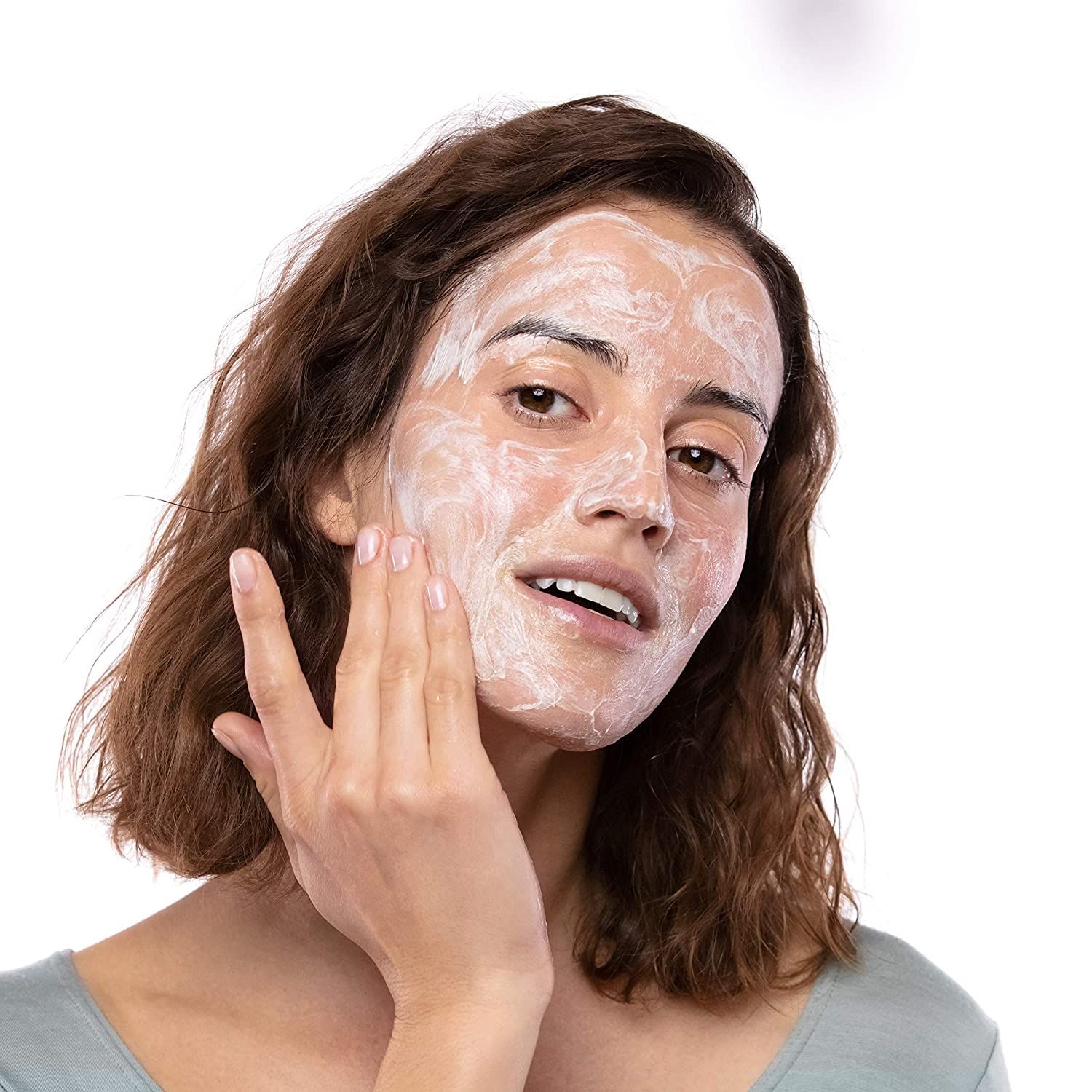 Femme appliquant du gel lavant sur son visage. Visage couvert de mousse blanche. Fond: blanc.