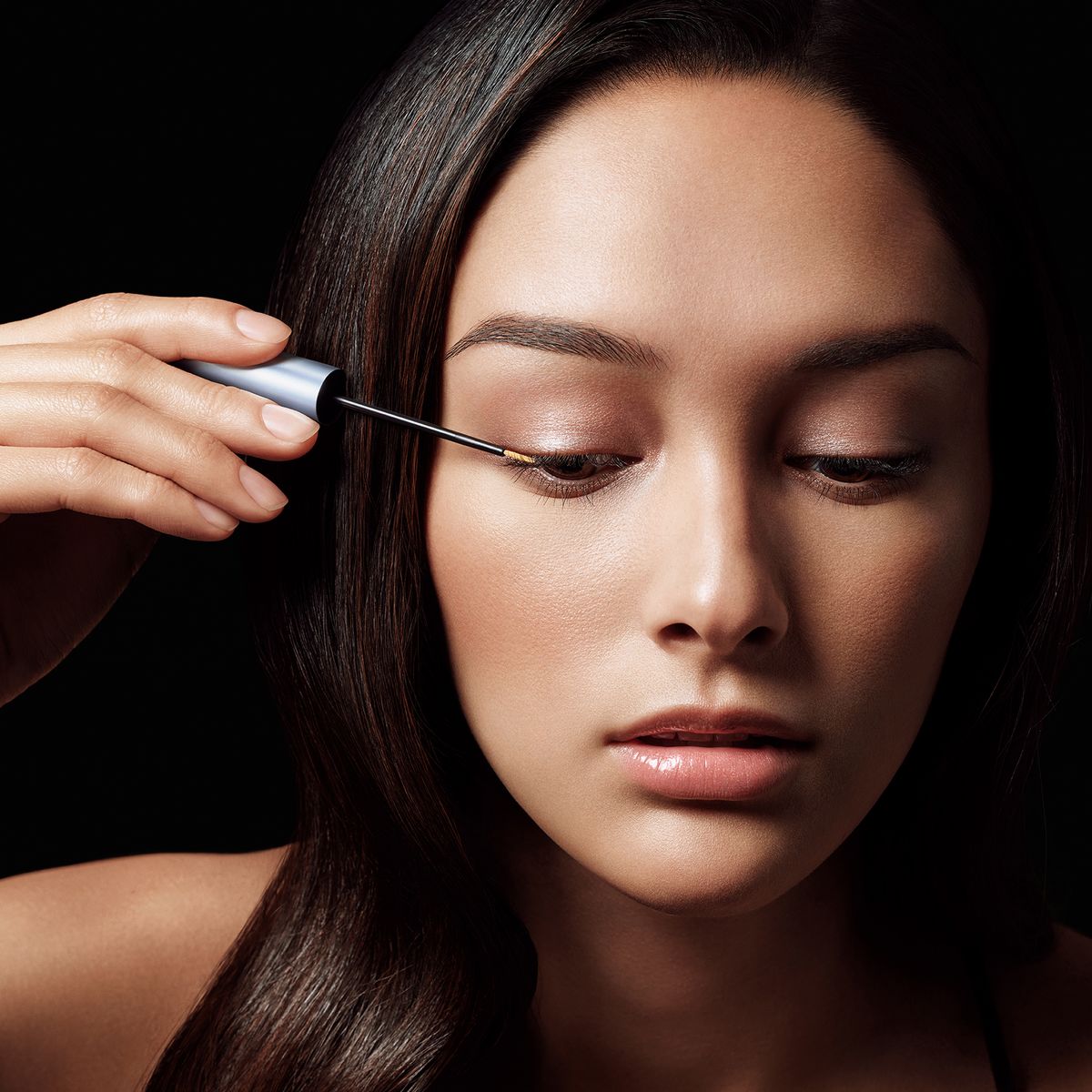 Vrouw brengt product aan met applicator. Zwarte achtergrond. Focus op oog.