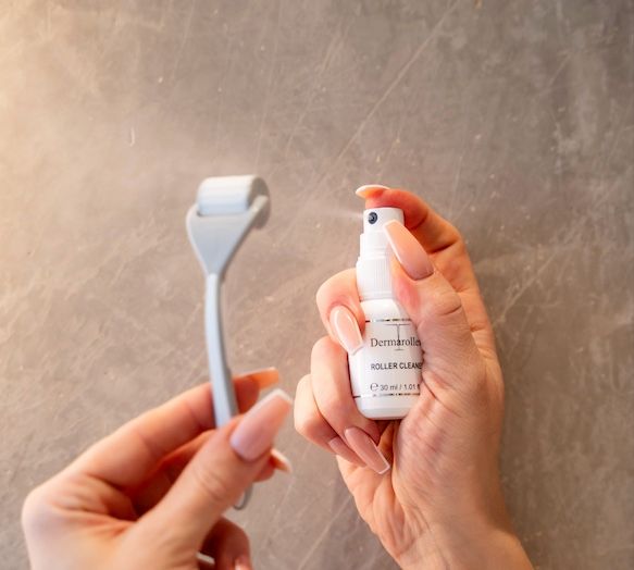 Handen houden Dermaroller en spuitfles vast. Fles met opschrift Roller Cleaner. Roller grijs, fles wit.