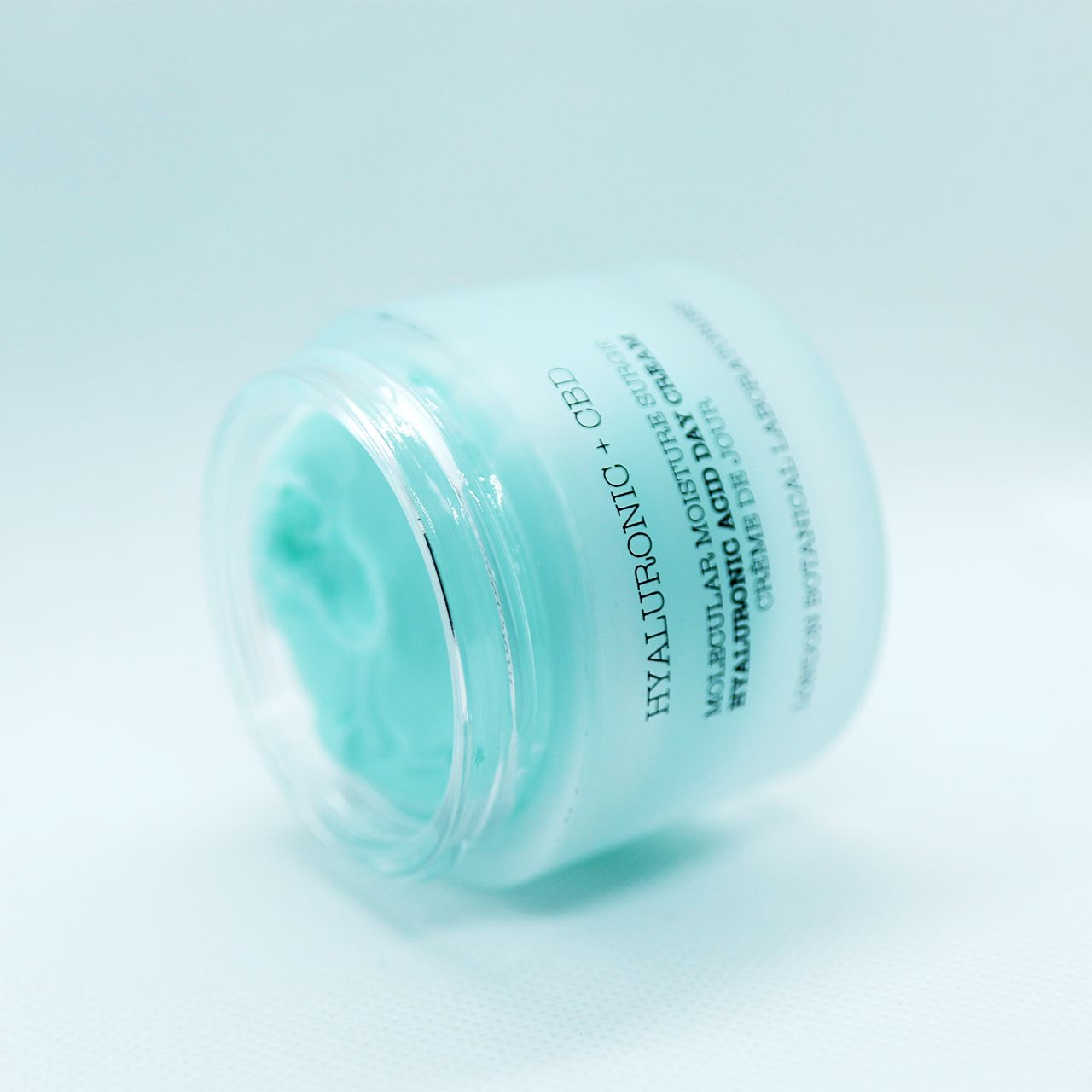 Schuin geplaatste pot met Hyaluronzuur + CBD vochtinbrengende crème. Blauwe pot met zilveren deksel.