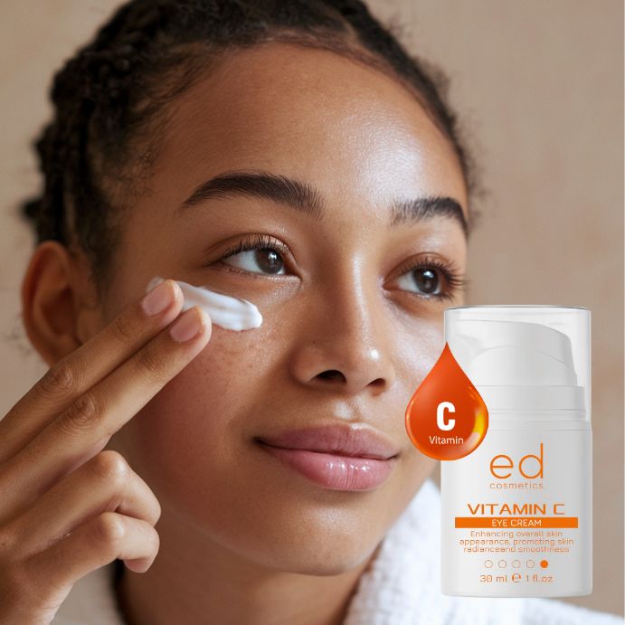 Femme appliquant de la crème pour les yeux. Flacon de crème pour les yeux blanc avec étiquette orange. Texte : Vitamin C Eye Cream, 30 ml, 1 fl.oz. Marque : ed cosmetics.