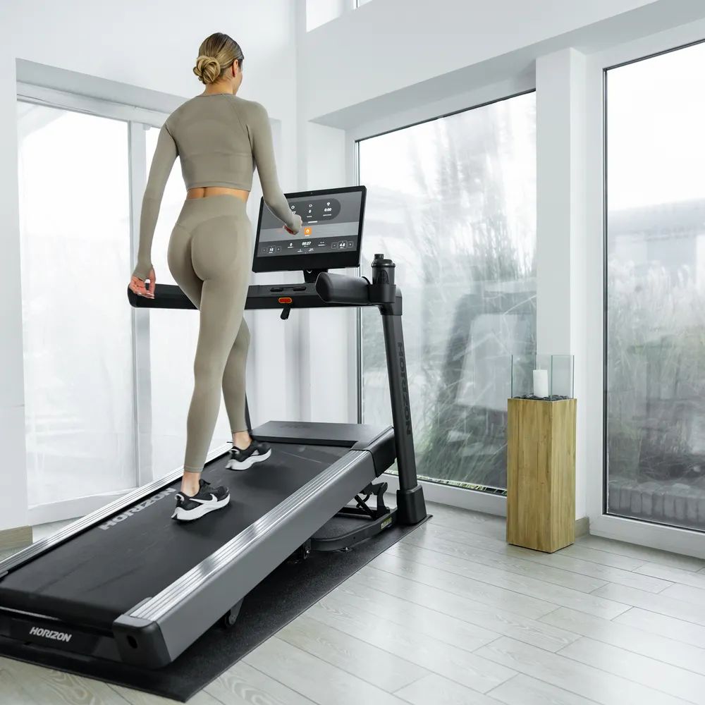 Femme marchant sur un tapis roulant. Tapis roulant noir avec écran. Logo Horizon visible.