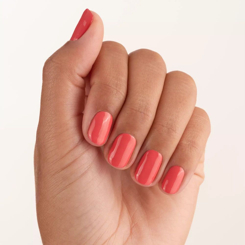 Main avec ongles vernis couleur corail. Tous les doigts sont vernis.