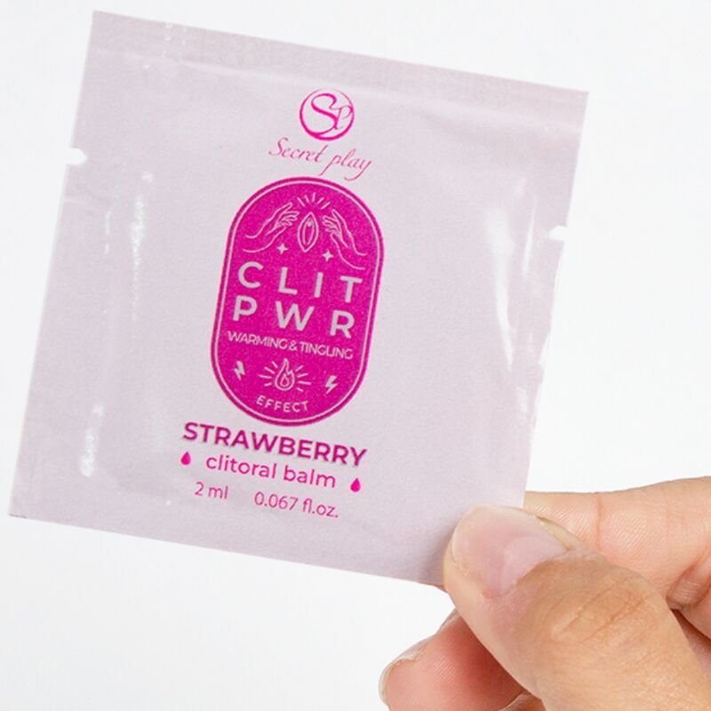 Roze zakje met tekst: CLIT PWR, Strawberry, clitoral balm. Merk: Secret Play. Vastgehouden door een hand.
