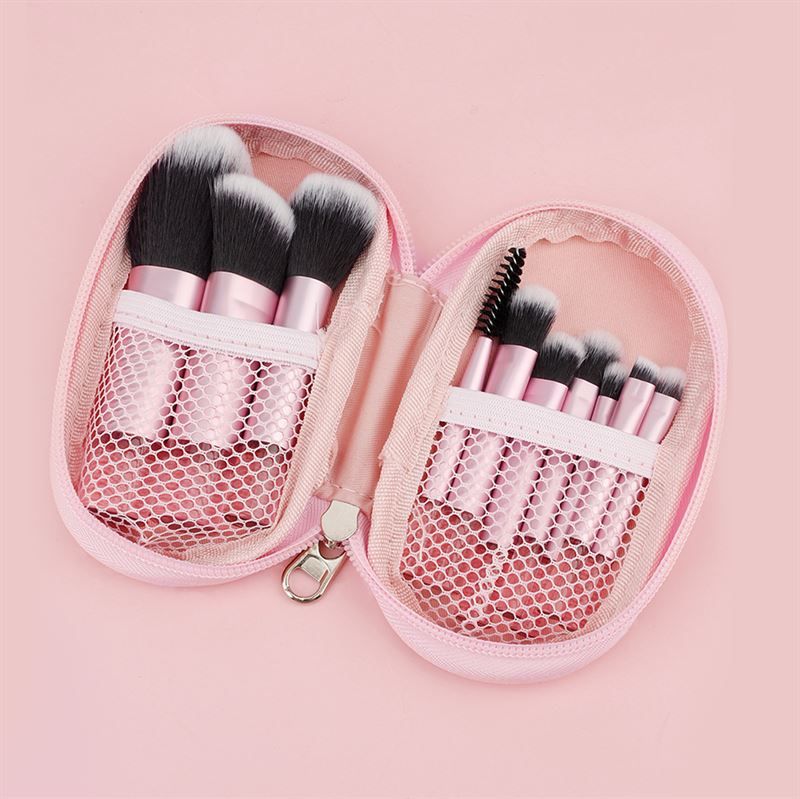 Trousse de maquillage rose zippée, ouverte. Contient des pinceaux avec manches roses et poils noirs. Compartiments en filet.