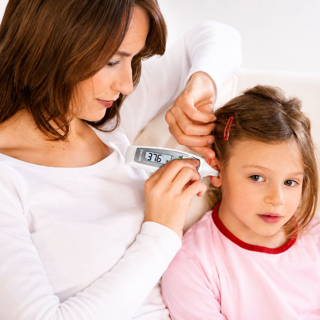 Une femme mesure la température d'un enfant avec un thermomètre auriculaire numérique. Le thermomètre affiche 37,6.