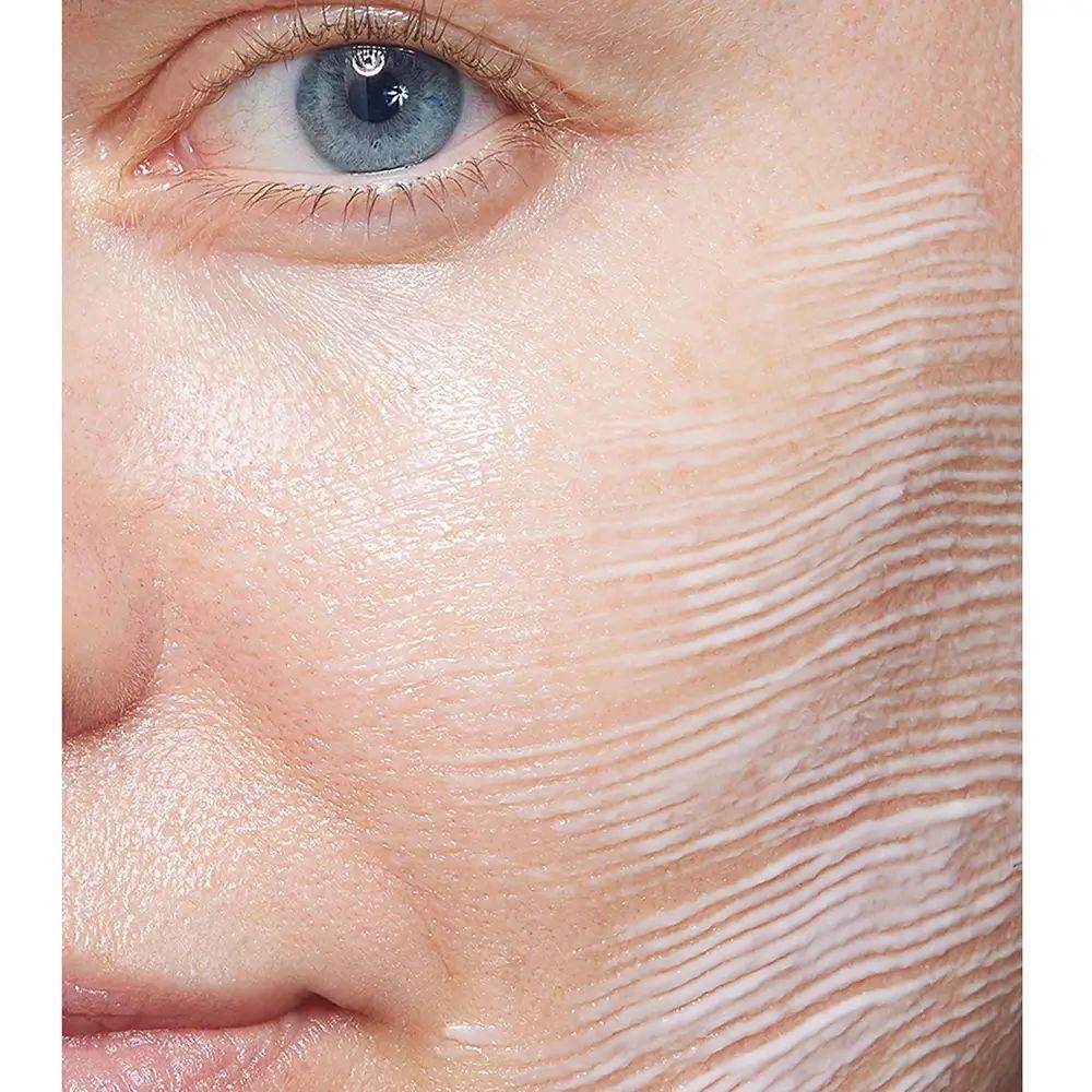 Gezicht van een persoon met aangebrachte crème. Crème in strepen op de huid. Oogcontour en helft van het gezicht zichtbaar.