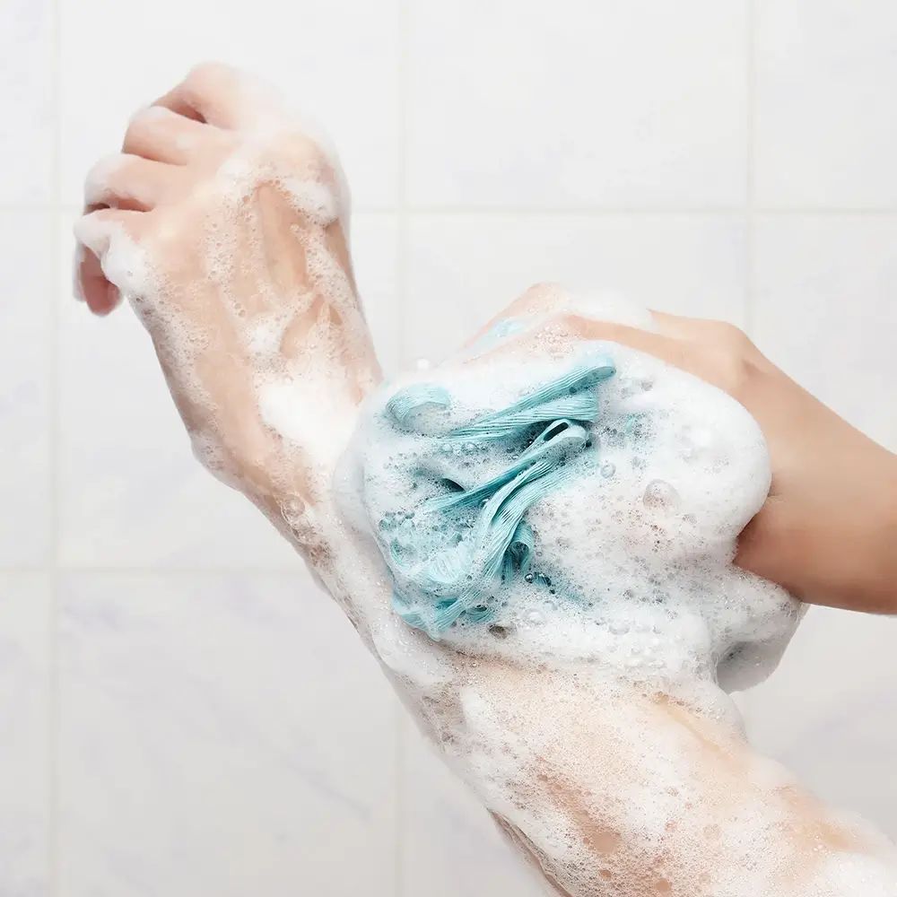 Handen met schuim en blauwe spons. Achtergrond: tegels. Schuimtextuur.