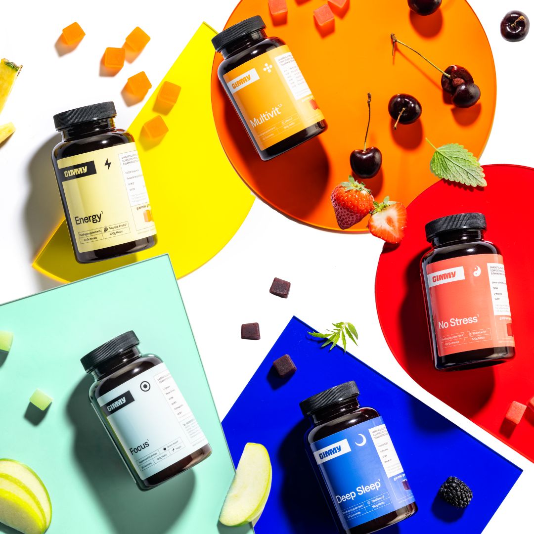 GIMMY Originals voedingssupplementen, vijf flessen en gummibeertjes. Op gekleurde achtergronden, met fruit.