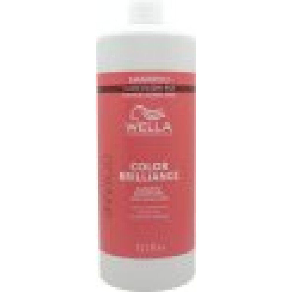 Haut flacon de shampooing blanc avec étiquette rouge. Texte: Wella, Color Brilliance, Shampoo. 1L. Pour cheveux colorés.