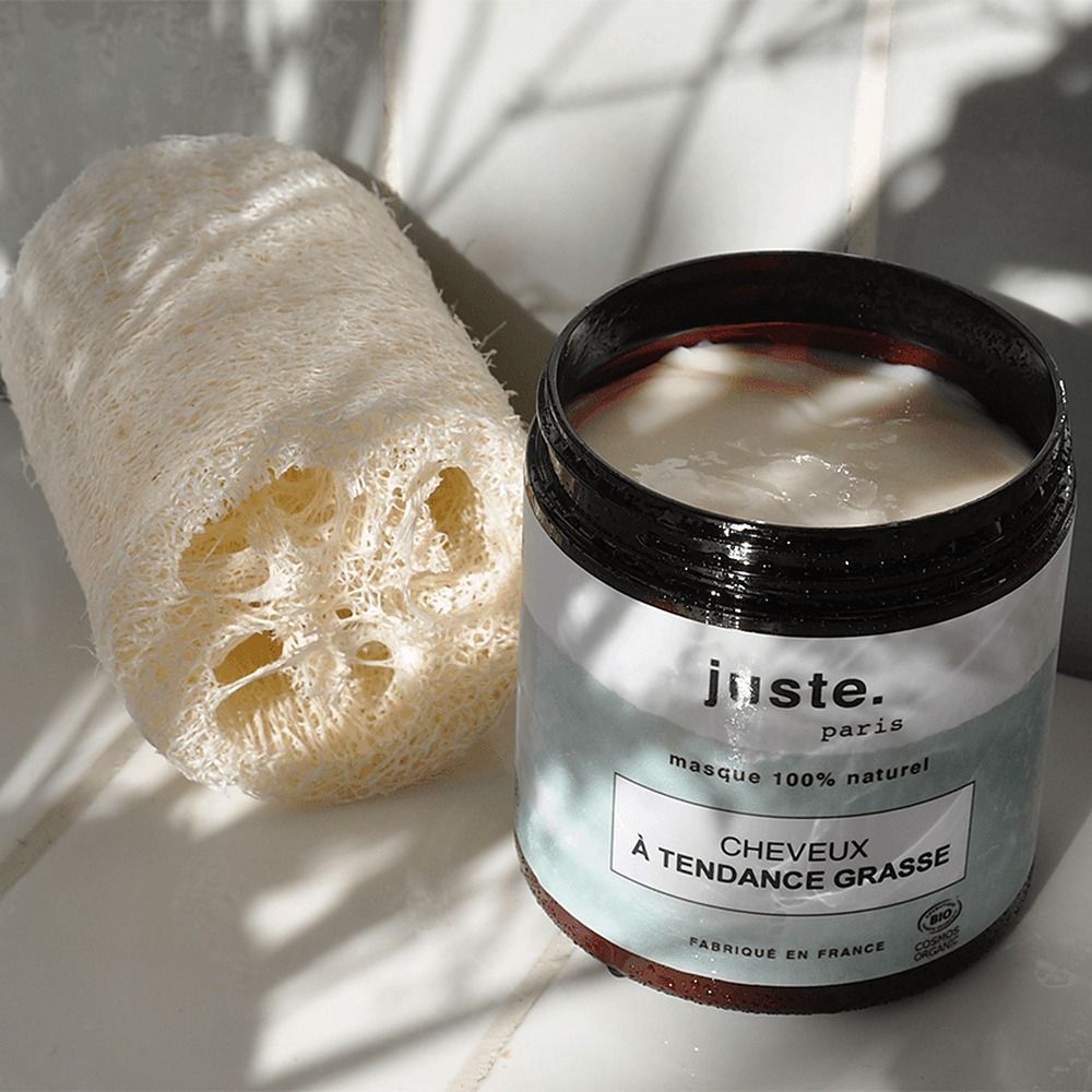 Een pot met witte crème en een loofah spons liggen naast elkaar.