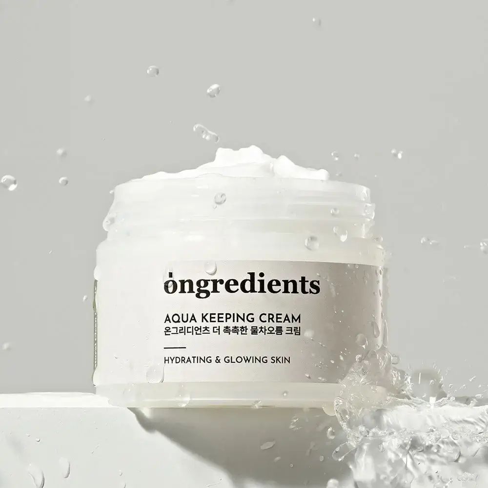 Pot de crème avec couvercle argenté, entouré d'eau. Inscription : Ongredients, Aqua Keeping Cream, Hydrating & Glowing Skin.