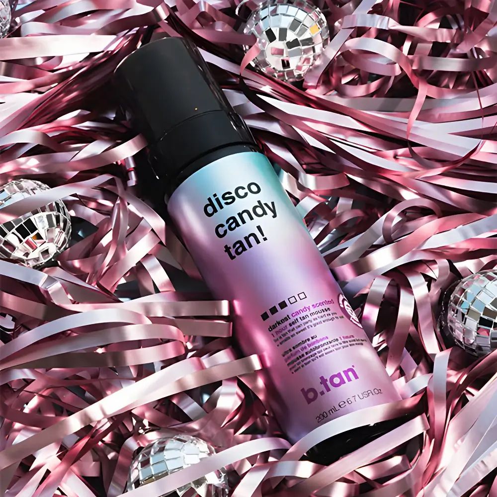 Fles zelfbruinende mousse met zwarte sproeikop. Tekst: Disco Candy Tan! en b.tan. Op roze confetti en discoballen.