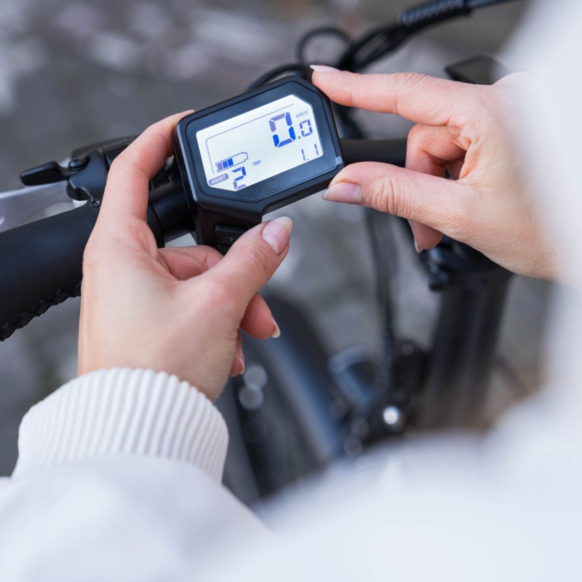 Handen houden een display vast. Zwart frame, wit scherm met cijfers. Weergave van snelheid en batterij.