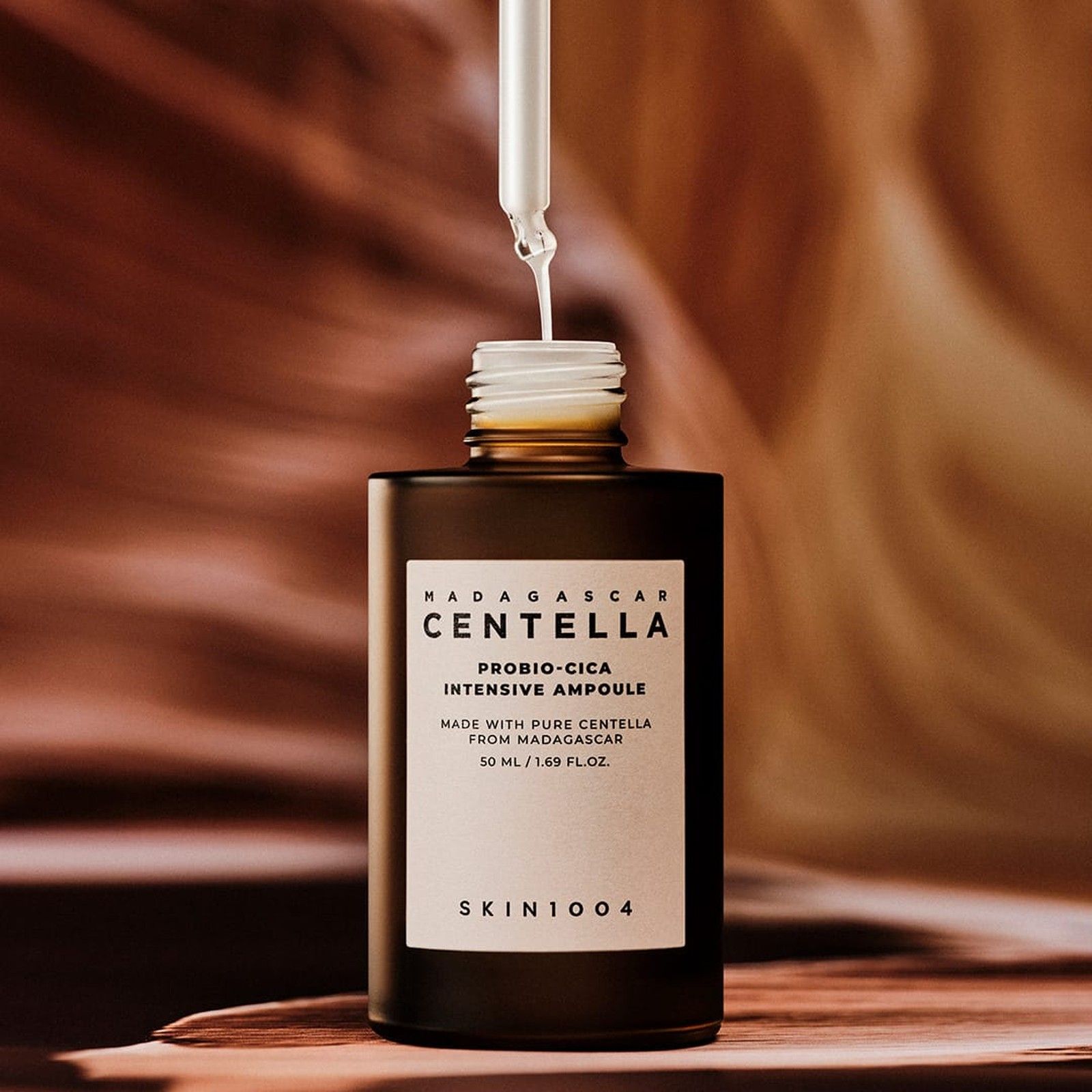 Een druppelaar laat serum in een geopende bruine fles vallen, etiket 'Centella Probio-Cica Intensive Ampoule'.