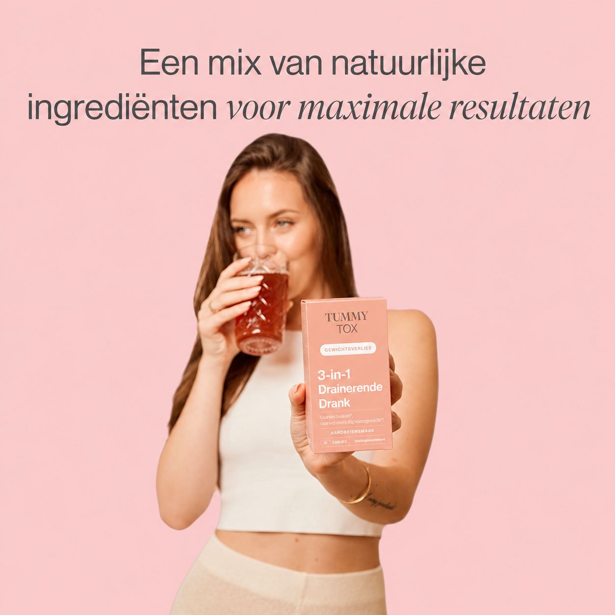 Vrouw houdt een pakje Tummy Tox 3-in-1 Drainerende Drank vast en drinkt uit een glas.