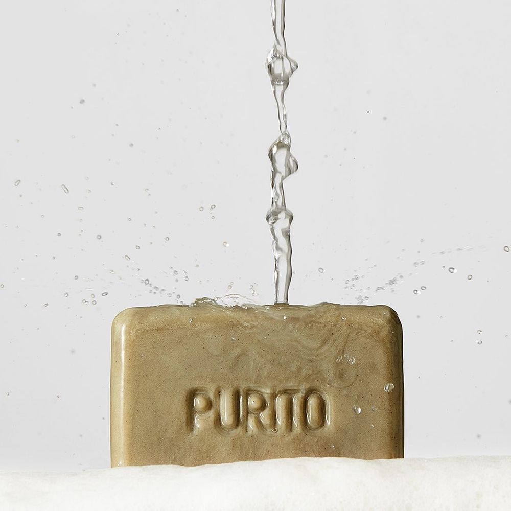 Savon sous l'eau courante. Le savon porte l'inscription « PURITO ».